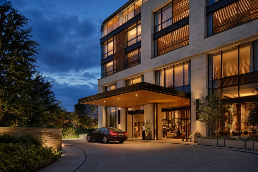 A hotel entrance at dusk - lit canopy, a car at the door and guests in the lobby