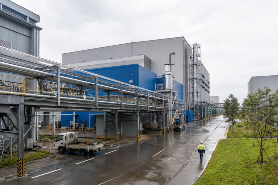 A process plant with pipe racks and a worker walking the site road